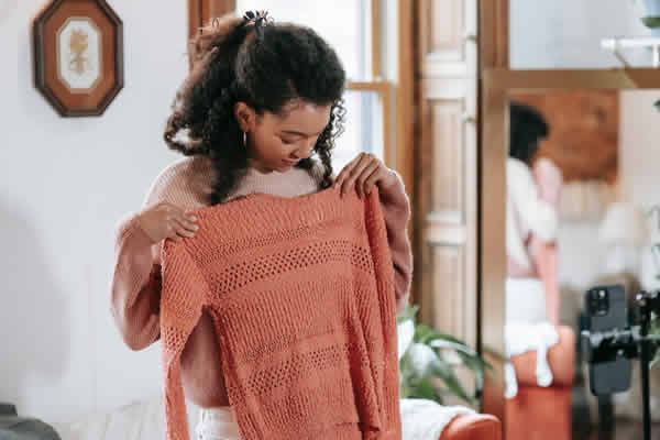 Una mujer probándose una remera tejida frente a una cámara. Reels de productos