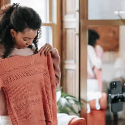 Foto: una mujer mostrando una remera tejida frente a una cámara.